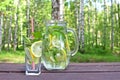 Lemonade drink in the glass jug with lemons, lime and mint on the wooden table outdoor.
