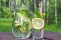 Lemonade drink in the glass jug with lemons, lime and mint on the wooden table outdoor.