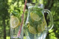 Lemonade drink in the glass jug with lemons, lime and mint on the wooden table outdoor.