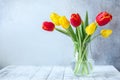 Fresh colorful tulips flowers bouquet in glass vase on wooden table In front of stone wall Royalty Free Stock Photo