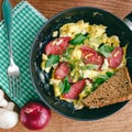 Fresh cooked scrambled eggs in pan with sausage and herbs. Bread, onion, mushrooms on wooden board, top view. Royalty Free Stock Photo