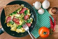 Fresh cooked scrambled eggs in pan with sausage and herbs. Tomato, chilli pepper, mushrooms on wooden board, top view. Royalty Free Stock Photo