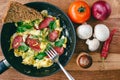 Fresh cooked scrambled eggs in pan with sausage and herbs. Tomato, onion, mushrooms on wooden board, top view Royalty Free Stock Photo