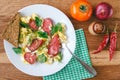 Fresh cooked scrambled eggs with sausage and herbs in white plate. Tomato, chilli pepper, onion on wooden board top view Royalty Free Stock Photo