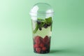 Fresh cool detox drink with Various berries in plastic cup on green background. Tasty infused water or lemonade to go. Proper Royalty Free Stock Photo