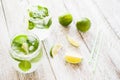 Fresh cool drinks with lime, mint and ice in glasses stand on a light wooden background.