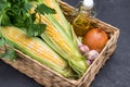 Fresh corn cobs, green parsley, oil in bottle, and garlic in wicker basket