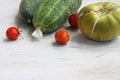 Fresh cracked green garden tomato with vertical splits along the sides, two cucumbers, three red cherry tomatoes on the white