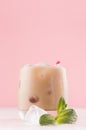 Fresh cream cocktail with ice cubes, green mint, striped straw on light pastel pink wall and white wood board, closeup, vertical. Royalty Free Stock Photo