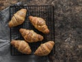 Fresh crispy croissants on a baking rack on a wooden background