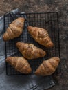 Fresh crispy croissants on a baking rack on a wooden background