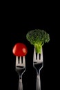 Tomato and broccoli on fork on black background, close up