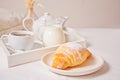 Fresh croissant bun on the white plate with cup of coffee, jar of milk on the wooden tray on the background Royalty Free Stock Photo
