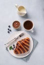 Fresh croissant with chocolate and blueberries on a white plate on a light background with a cup of black coffee and milk jug. Royalty Free Stock Photo