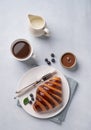 Fresh croissant with chocolate and blueberries on a white plate on a light background with a cup of black coffee and milk jug. Royalty Free Stock Photo