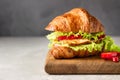 Fresh croissant sandwich with grilled chicken or turkey, bell pepper, sauce and salad leaves on wooden cutting board. Royalty Free Stock Photo