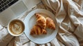 Fresh croissants and coffee on a white plate, with a laptop on bed