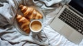 Fresh croissants and coffee on a white plate, with a laptop on bed