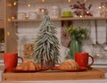 Fresh croissants on a plate, cups, Christmas tree on the background of Christmas kitchen Royalty Free Stock Photo