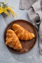 A fresh croissants in a wooden plate on a blue background with yellow flowers and napkin