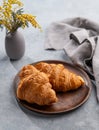 A fresh croissants in a wooden plate on a blue background with yellow flowers, napkin and morning light