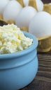 Fresh crumbly cottage cheese close-up on a dark table against the background of white eggs in a tray