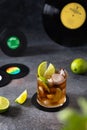 Fresh Cuba Libre cocktail with cola, lime and mint on dark background with vinil records. Alcoholic, non-alcoholic beverage.