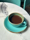 Fresh cup of coffee in a turquoise colored cup and saucer