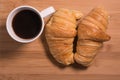 Fresh coffee in white cup next to a pair of French croissants on natural wood background Royalty Free Stock Photo