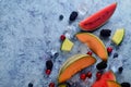 Fresh cut melon, watermelon, berries and ice cubes on a blue stone background. Copy space and text area