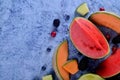 Fresh cut melons, watermelon and berries on a blue stone background