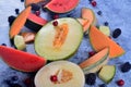 Fresh cut melons, watermelon and berries on a blue stone background