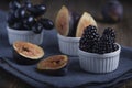 Fresh cuted organic figs, blackberry and grapes on white cupcake baking dish on rustic wooden background with dark blue napkin