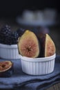 Fresh cuted organic figs, blackberry and grapes on white cupcake baking dish on rustic wooden background with dark blue napkin