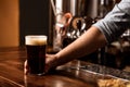 Fresh dark beer with foam in pub. Bartender gives glass to dark drink with foam on bar counter Royalty Free Stock Photo