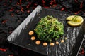 Fresh delicious Chukka seaweed Wakame salad ina black plate on a black stone background with limon and sauce
