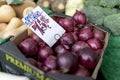 Fresh, delicious organic English red onions on a farmers market stall in the UK with a price sign saying 75p per half kilo