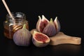 Fresh delicious young whole figs, sliced first on a wooden chopping board. A jar of honey with a spoon for honey in the background