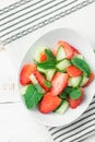 Fresh Detox Summer Spring Salad with Strawberries Green Mint Leaves in White Ceramic Bowl on Cotton Kitchen Towel. Wood Table