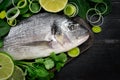 Fresh dorada fish with herbal, onion, parsley and lime on a cutting board on black background Royalty Free Stock Photo