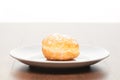 Fresh doughnut with icing sugar on white ceramic plate on bright light brown wooden table