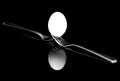 Diagonal view of white egg balanced on two forks with reflections on black background