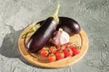 Fresh eggplant, a head of garlic and a branch of cherry tomatoes on a round wooden cutting board Royalty Free Stock Photo