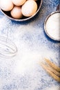Fresh eggs in a bowl, eggbeater, wheat on flour background. Top view. Copy space. Royalty Free Stock Photo