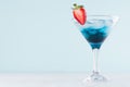 Fresh exotic alcohol drink with blue liquor curacao, strawberry, ice cubes in wineglass on elegant blue pastel color background. Royalty Free Stock Photo