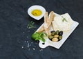 Fresh feta cheese with olives, basil, rosemary and bread slices on white ceramic serving board over black slate stone Royalty Free Stock Photo