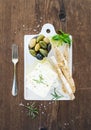 Fresh feta cheese with olives, basil, rosemary and bread slices on white ceramic serving board over rustic wooden Royalty Free Stock Photo