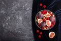 Fresh figs, strawberries and raspberries on blue plate on black concrete background and blue velvet textile. top view Royalty Free Stock Photo