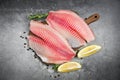 Fresh fish fillet sliced for steak or salad with herbs spices rosemary and lemon - Raw tilapia fillet fish and salt on dark stone