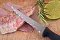 Knife on raw red mullet fillets laid on a cutting board with a slice of lemon and rosemary close-up